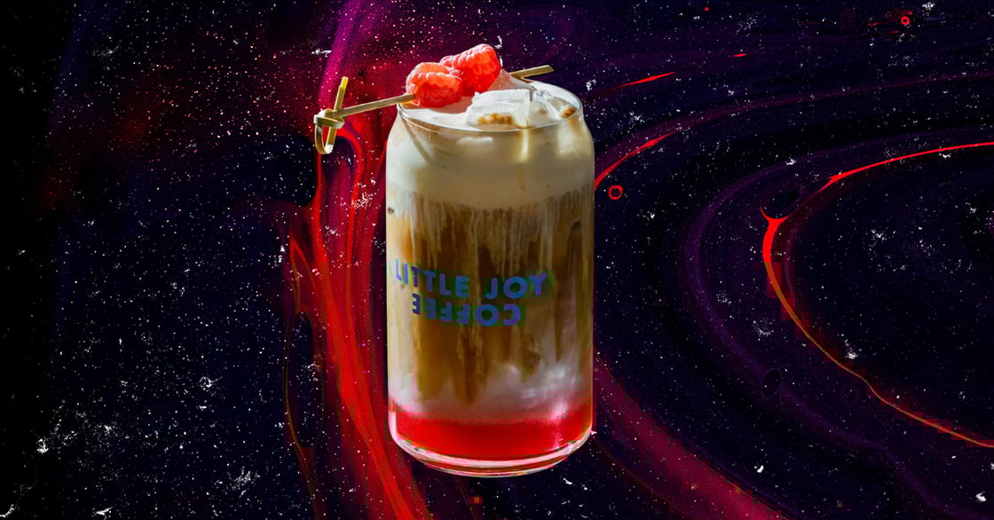 A raspberry danish latte from Little Joy Coffee in a branded glass.