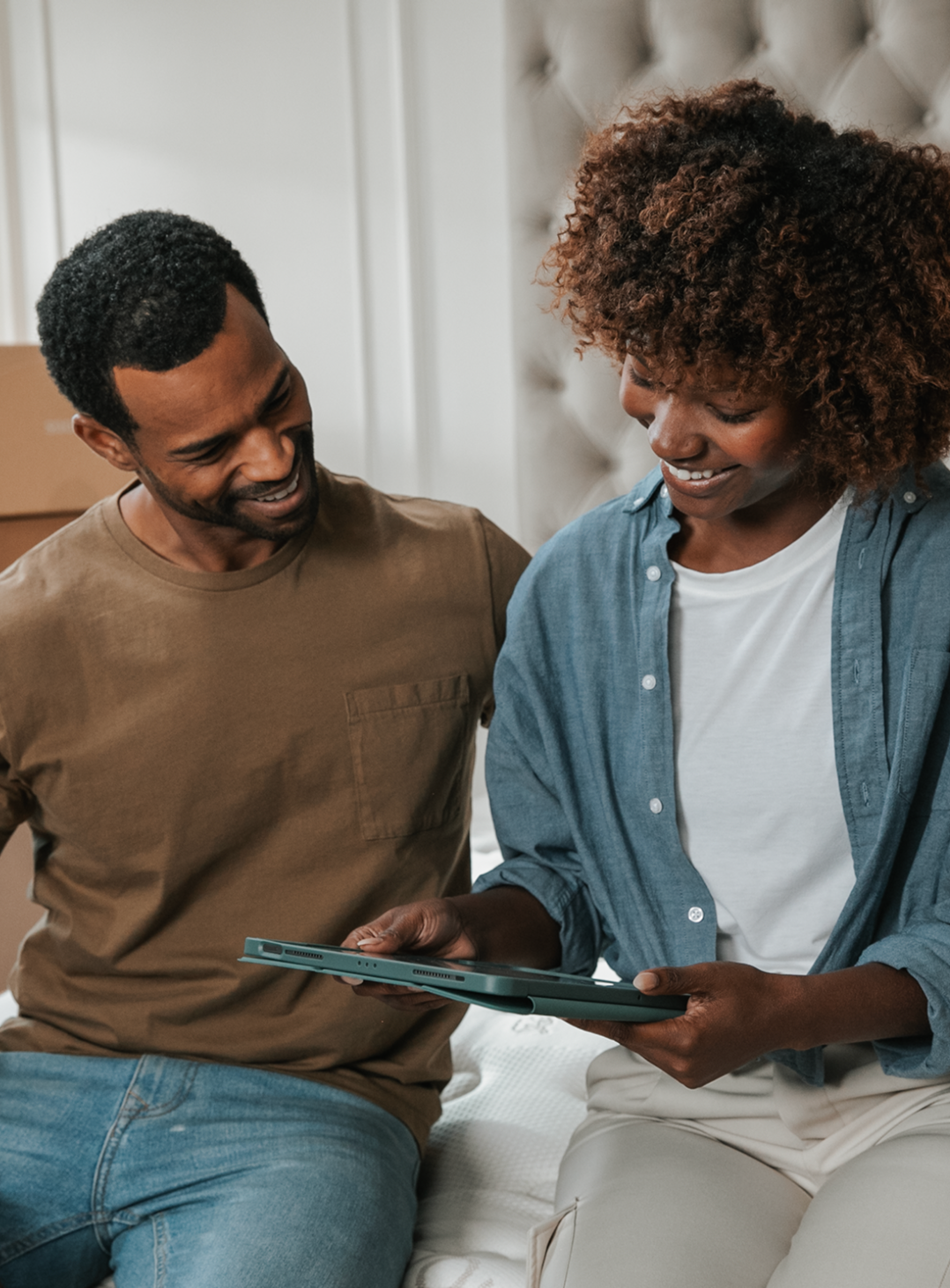 Man and woman sitting on a bed looking at a tablet