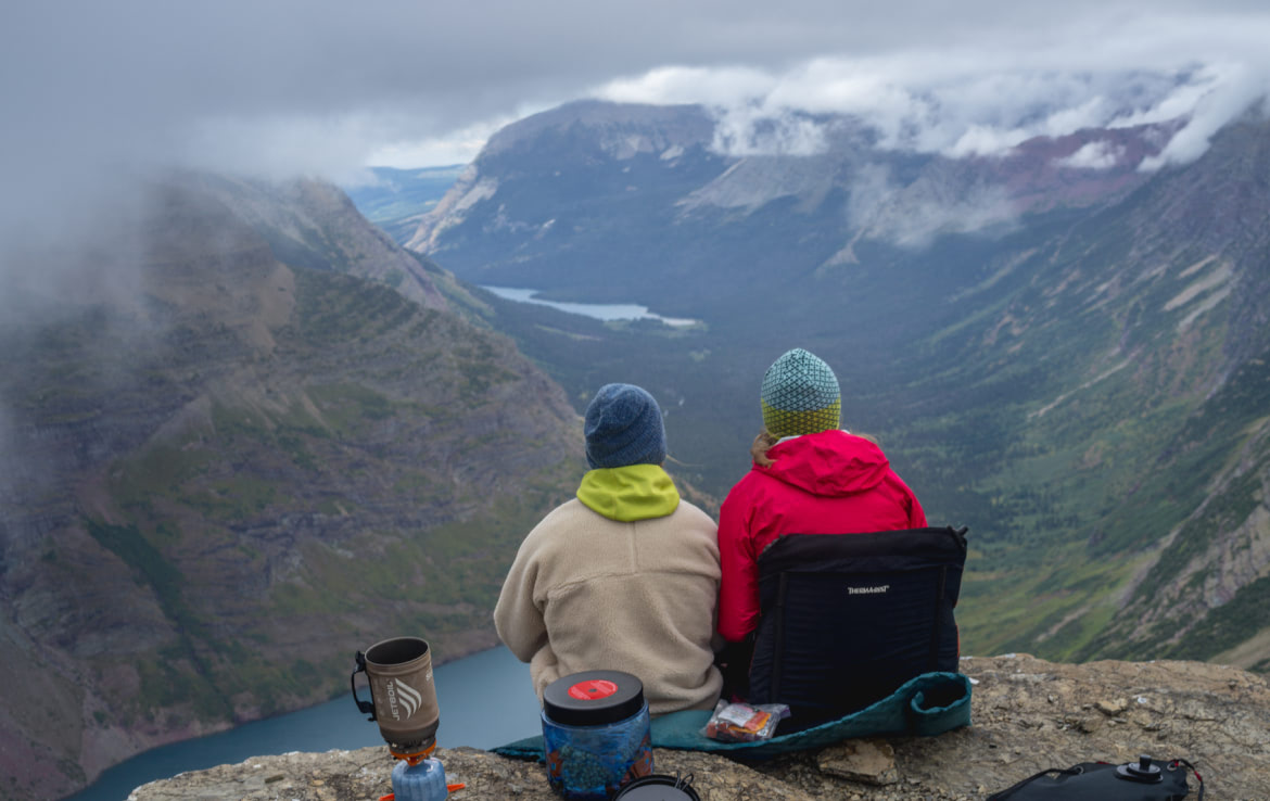 Two hikers sit side by side overlooking a glacial valley.
