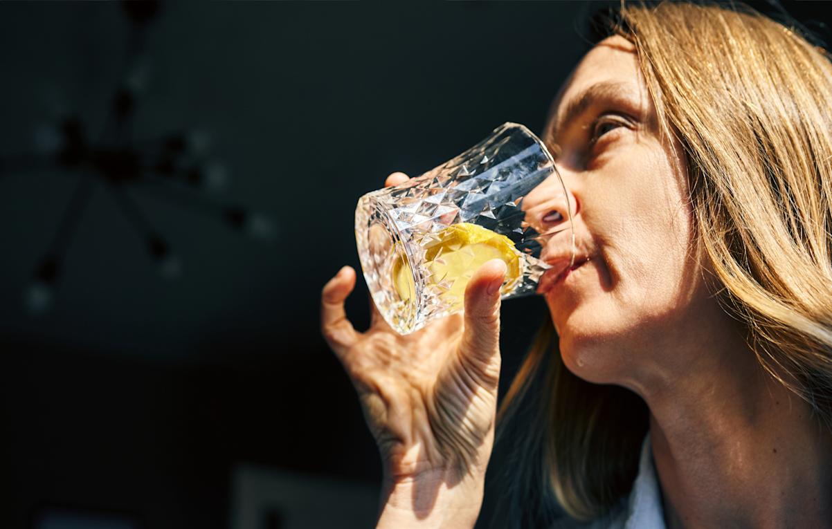 Woman Drinking Lemon Water From Cut Glass Tumbler At Home In Morning Sunlight 