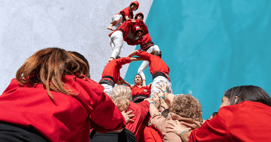 Several people in white pants and red jackets building a human tower.